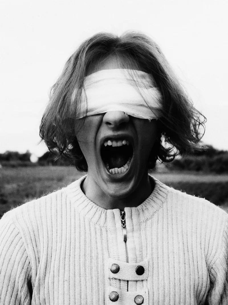 Schwarzweißfoto: ein Mensch mit verbundenen Augen schreit mit weit offenem Mund
