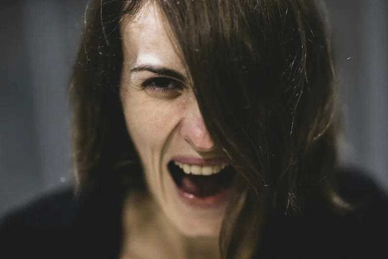 Eine Frau mit dunklen Haaren, die ihr halb ins Gesicht fallen, schreit mit verzerrtem Gesicht in die Kamera