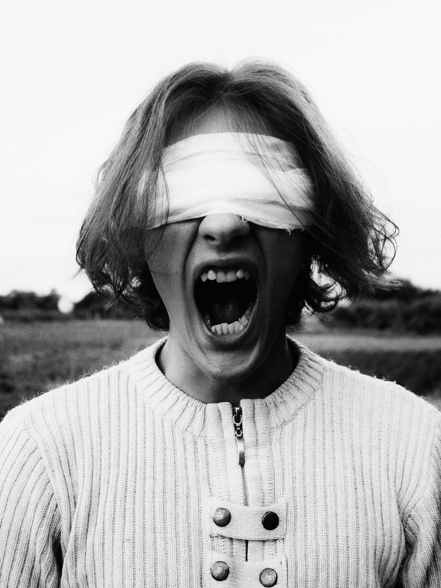Schwarzweißfoto: ein Mensch mit verbundenen Augen schreit mit weit offenem Mund